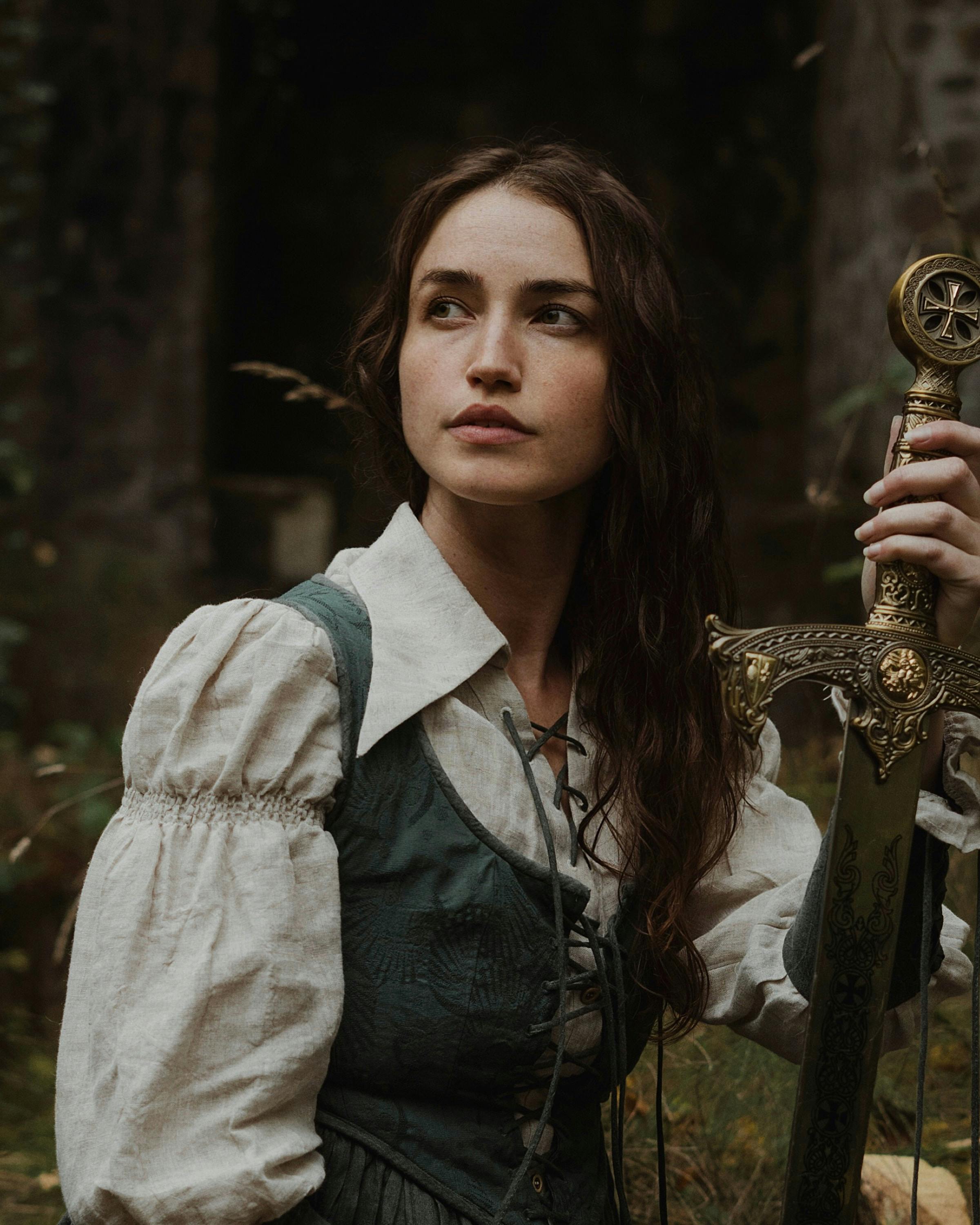 Portrait of a woman with a medieval look, holding a sword in an outdoor setting, exuding strength and elegance.